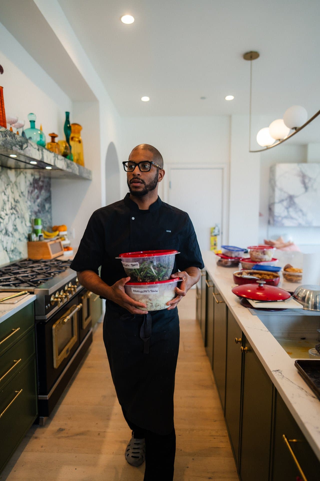 A Sous chef walking through a customer's kitchen carrying labeled meal-prep containers