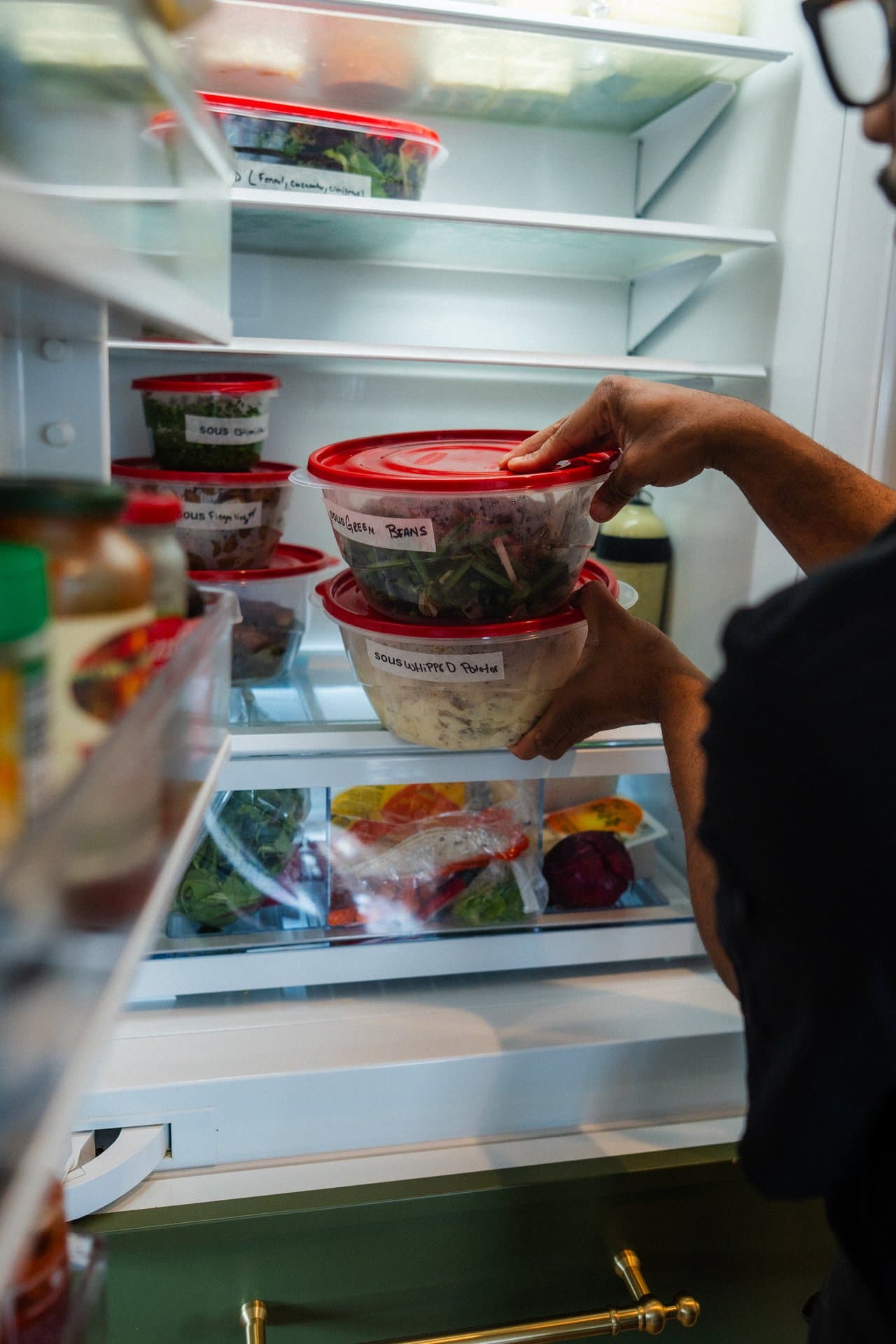 A chef loading labeled SOUS meal-prep containers into a customer's fridge